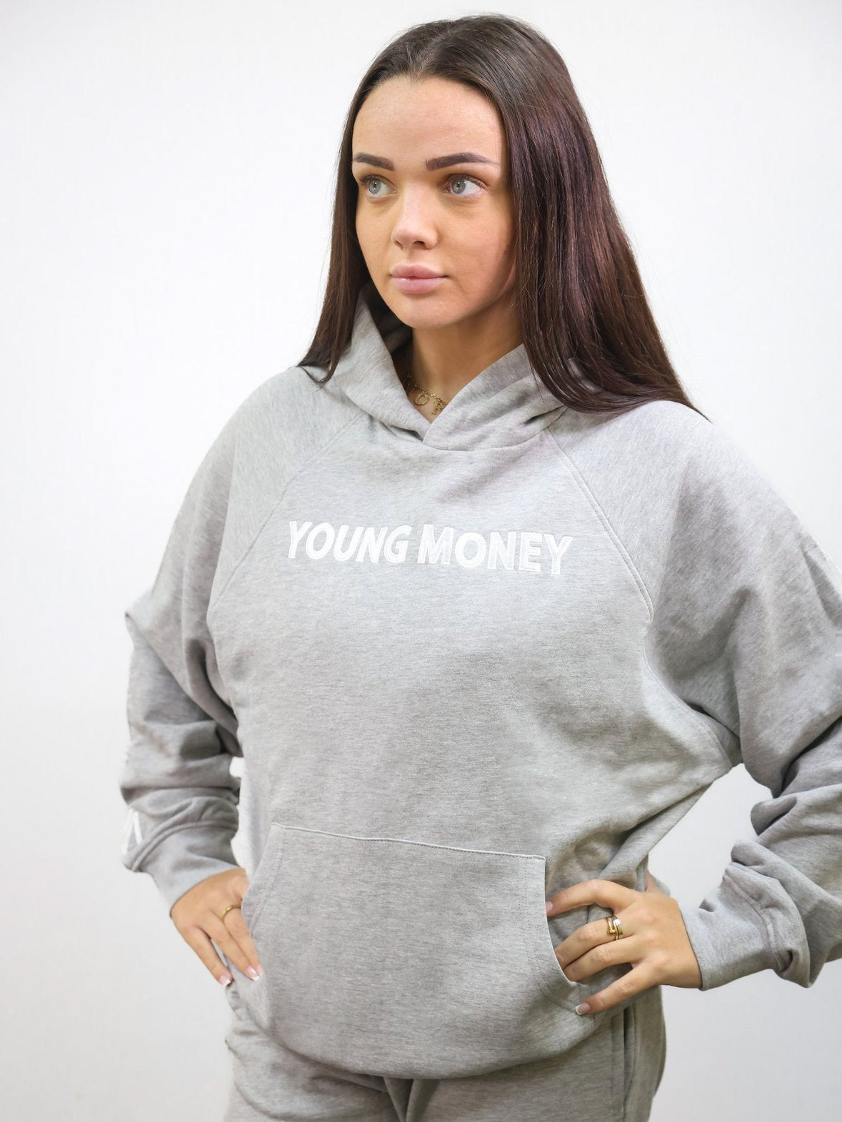 Grey organic cotton oversized hoodie with white embroidered young money text to the front and white embroidered logo on the sleeve on a female model size XS