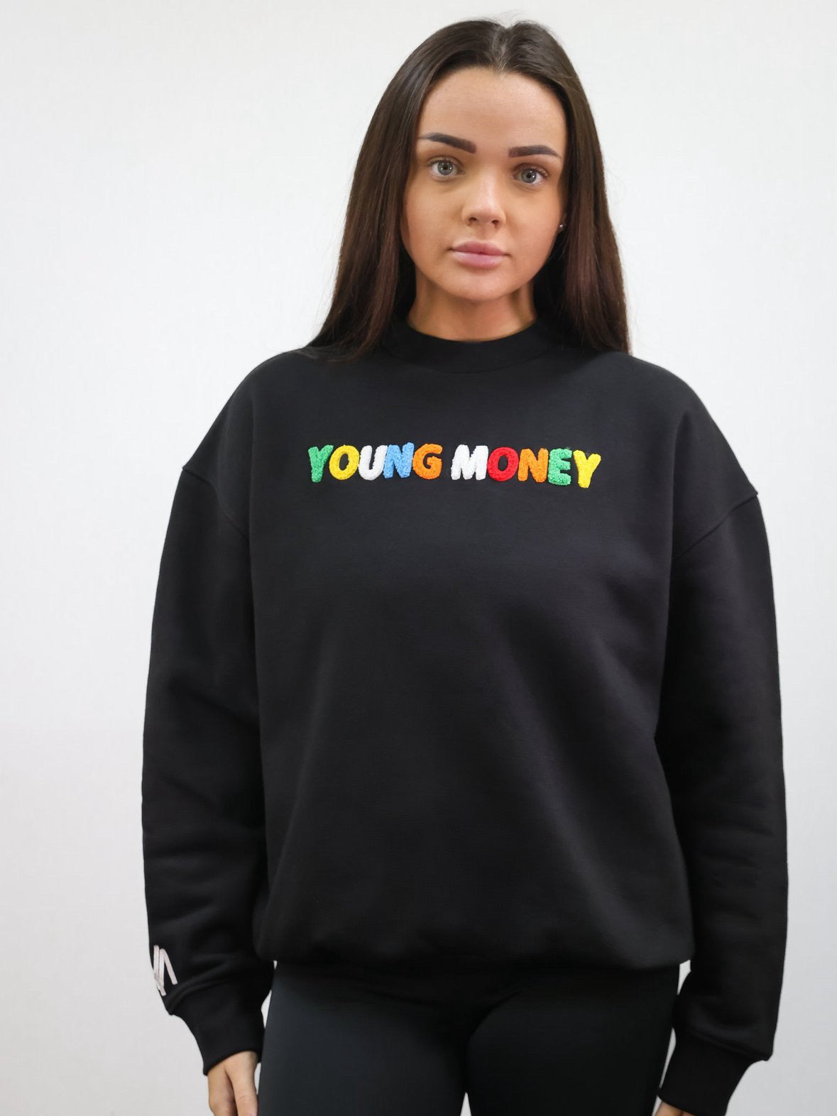 Black sweatshirt with a fluffy embroidered young money text in illuminous multicolours and a white embroidered logo on the sleeve on a female model size small