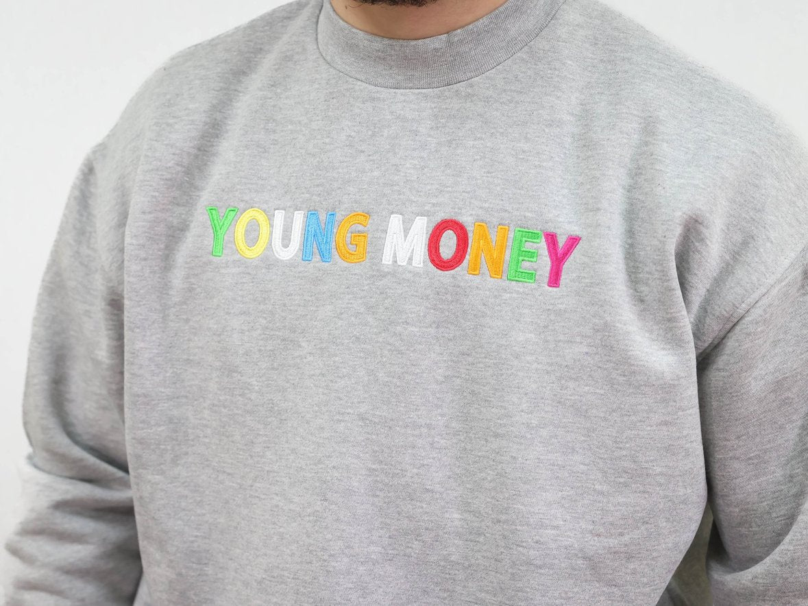 Grey sweatshirt with a direct embroidered young money text in illuminous multicolours close up image worn by a male model 