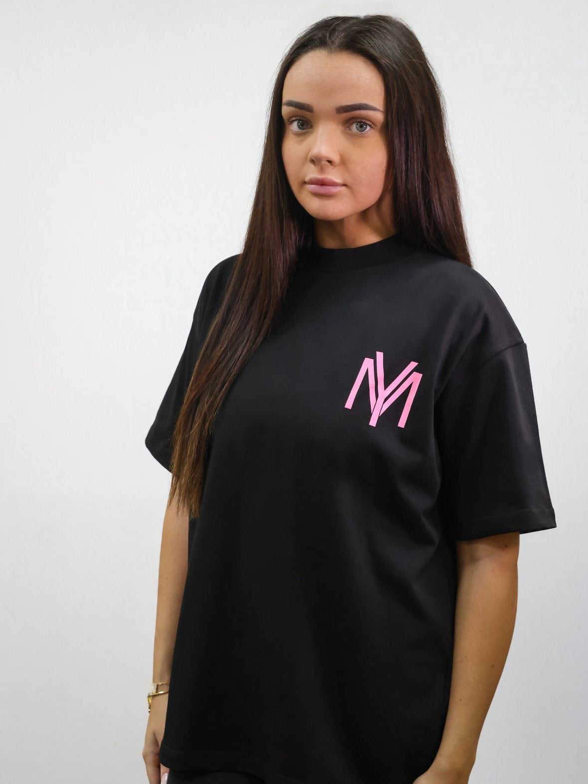 Black organic cotton oversized T-shirt featuring a printed pink YM logo on the front on a female model size XS