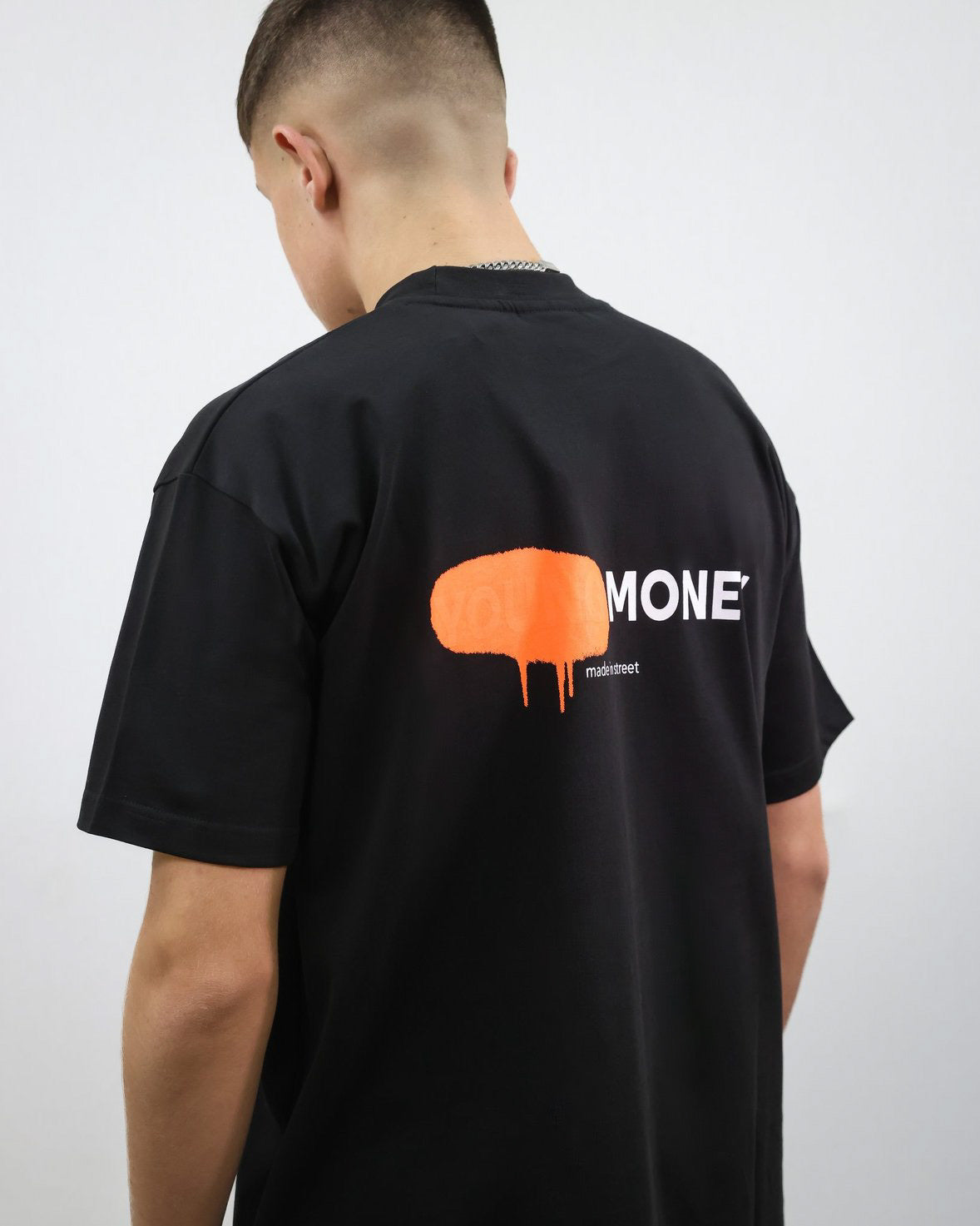 Black organic cotton oversized T-shirt with an orange spray paint graphic on the back on a male model size small