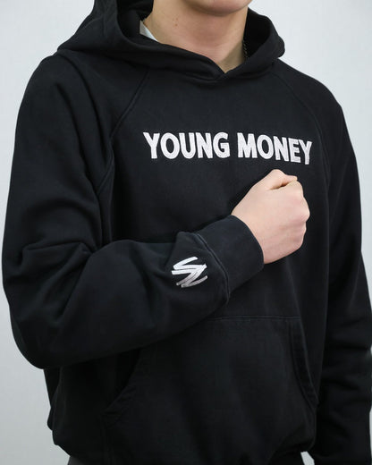 Black organic cotton oversized hoodie with white embroidered young money lettering on the front and a white embroidered YM logo on the sleeve on a male model size small 