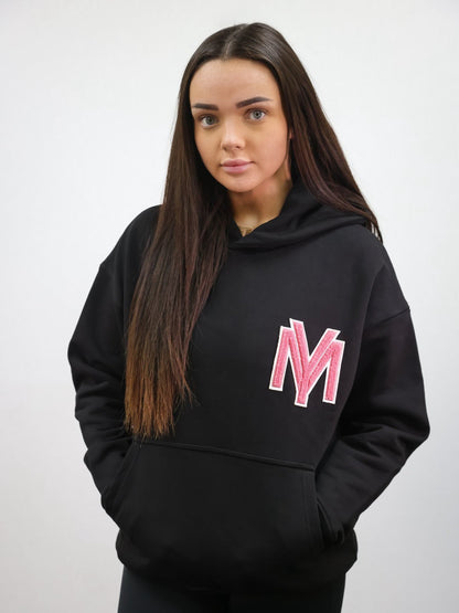 Premium organic cotton black hoodie with a raised fluffy embroidered YM logo on the chest in pink on a female model size small