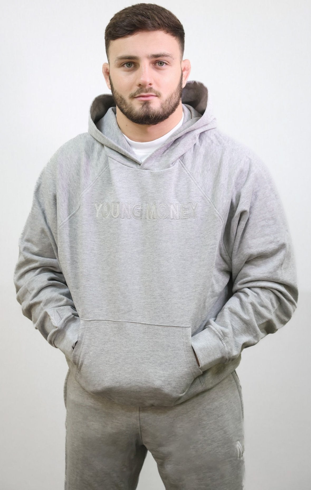 All grey organic cotton tracksuit featuring matching oversized hoodie and joggers with embroidered logo and text on a male model size small