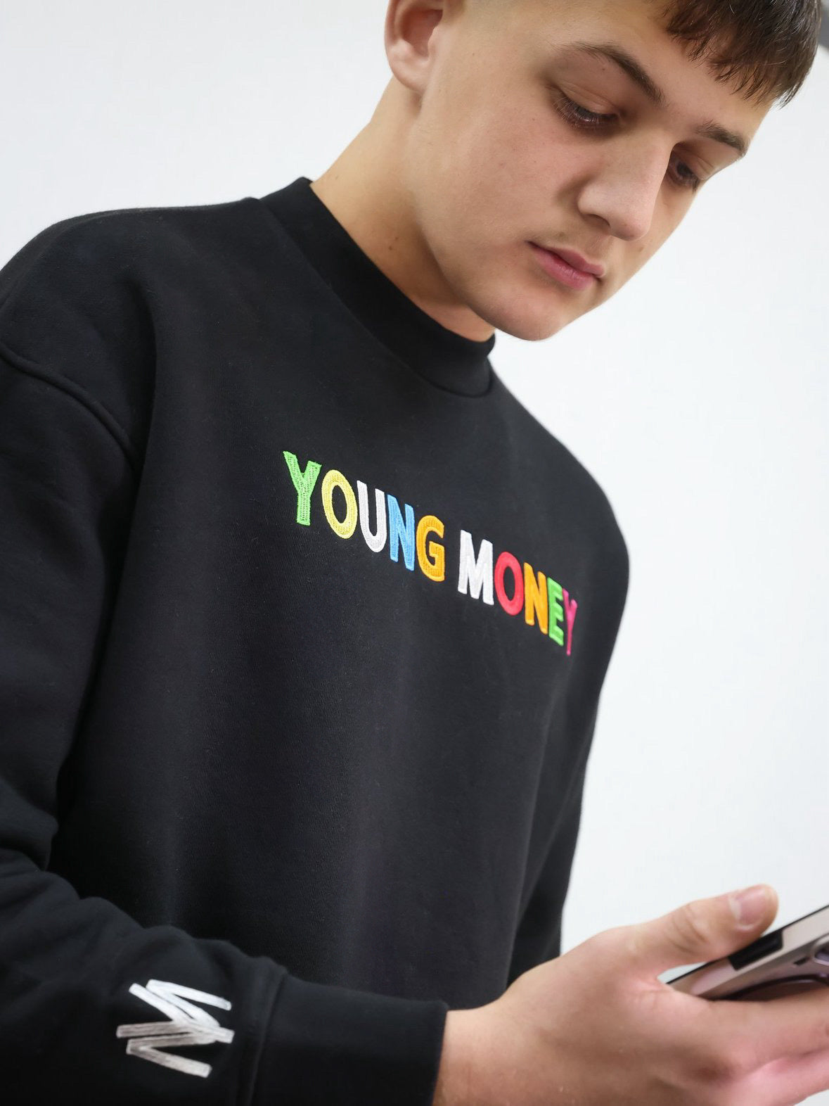 Black sweatshirt with a direct embroidered young money text in illuminous multicolours and white embroidered logo on the sleeve on a male model size medium