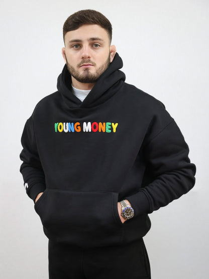 Black hoodie with a fluffy embroidered young money text in illuminous multicolours and a white embroidered logo on the sleeve on a male model size medium