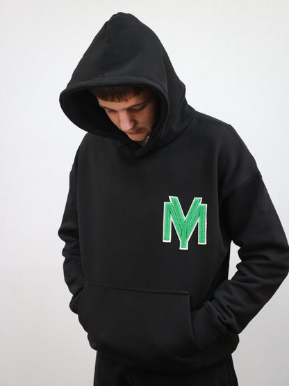 Premium organic cotton black hoodie with a raised fluffy embroidered YM logo on the chest in green on a male model size medium