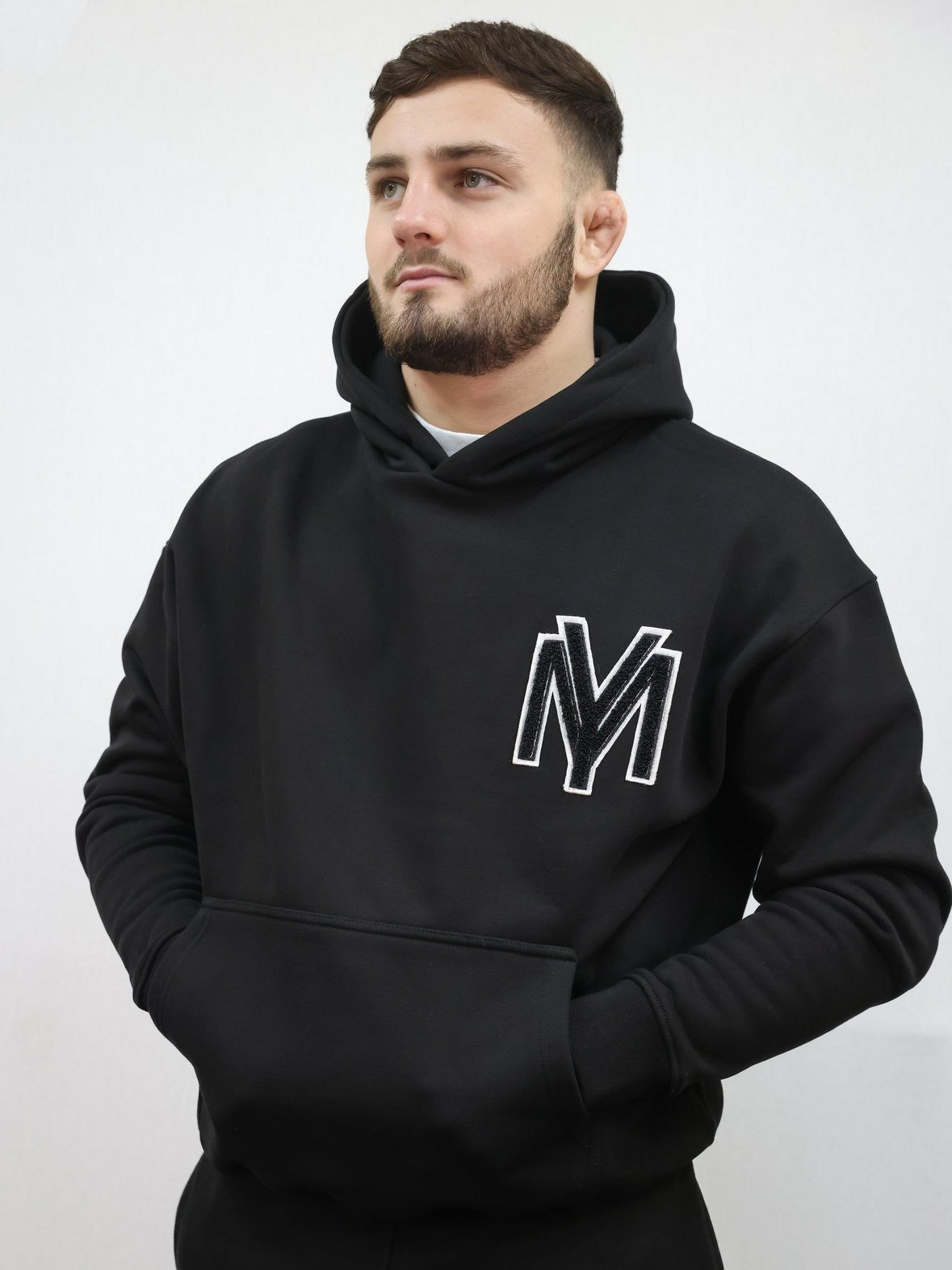 Premium organic cotton black hoodie with a raised fluffy embroidered YM logo on the chest in black on a male model size medium