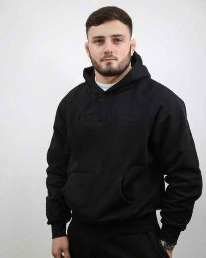 Premium organic cotton black hoodie with a black embroidered Young Money text across the front on a male model size small 