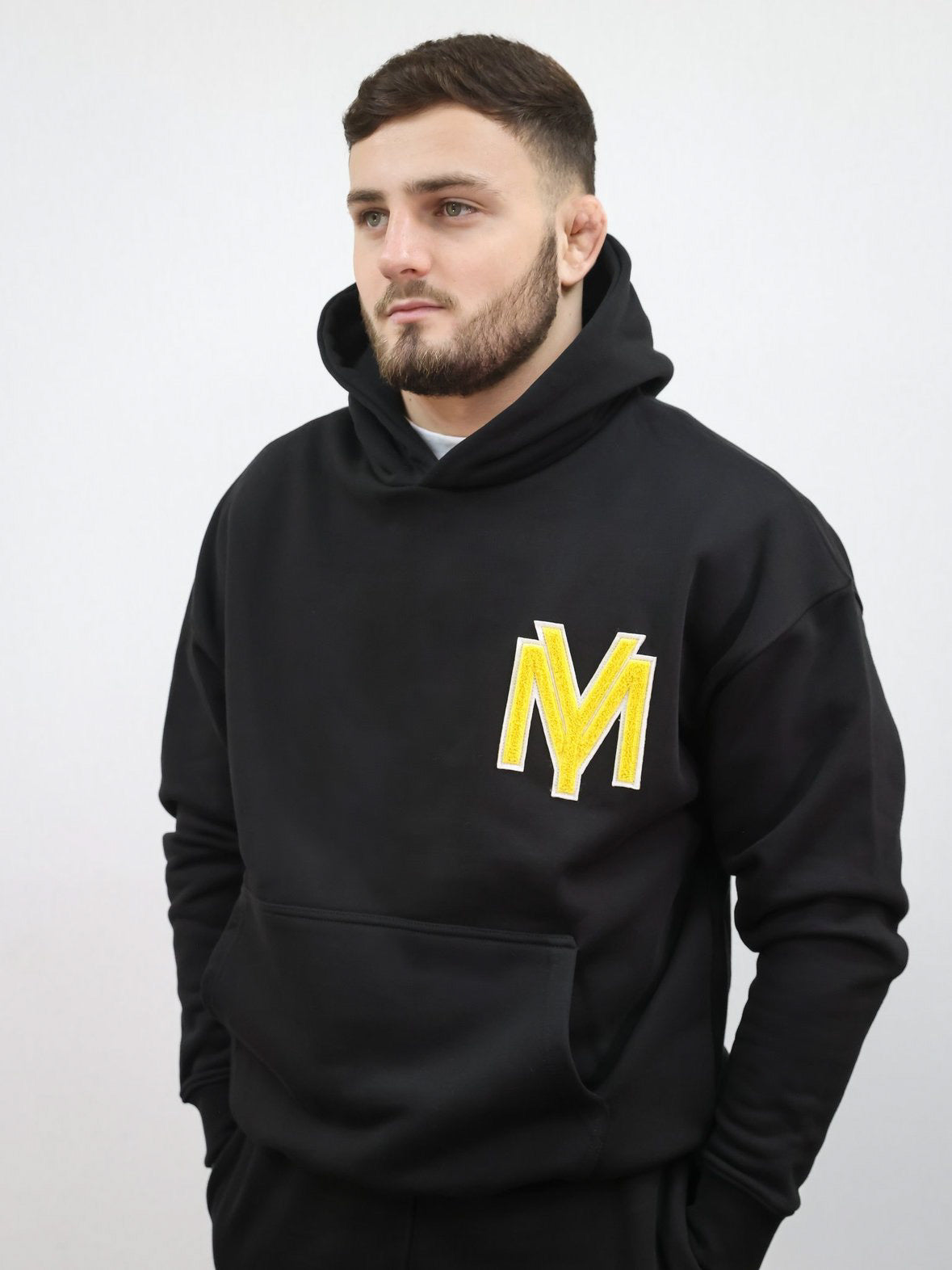 Premium organic cotton black hoodie with a raised fluffy embroidered YM logo on the chest in yellow on a male model size medium